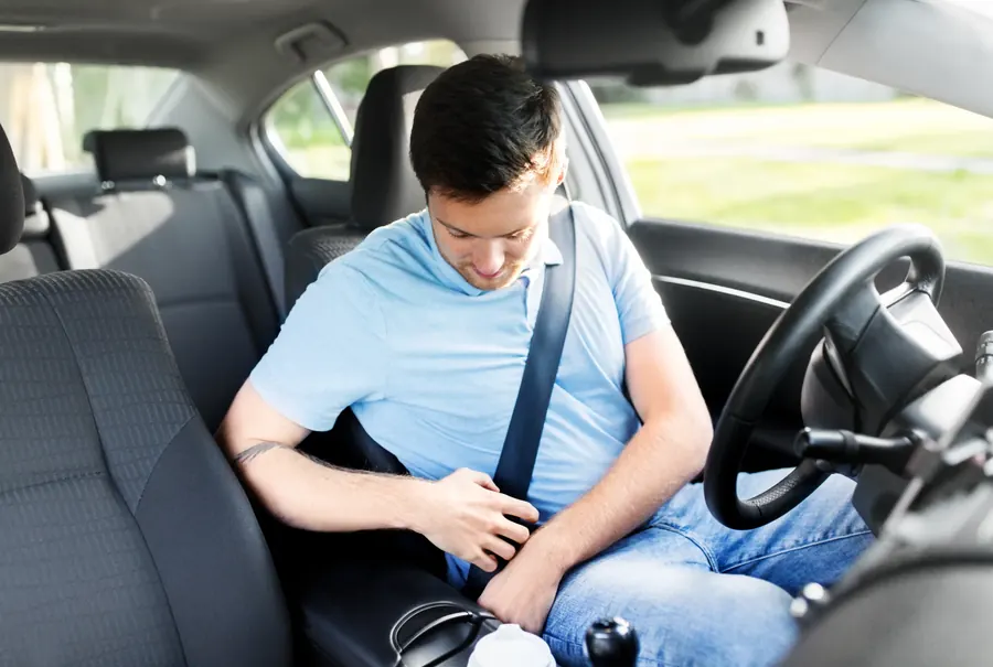 A driver seated in a car interior fastening the seatbelt buckle at the hip