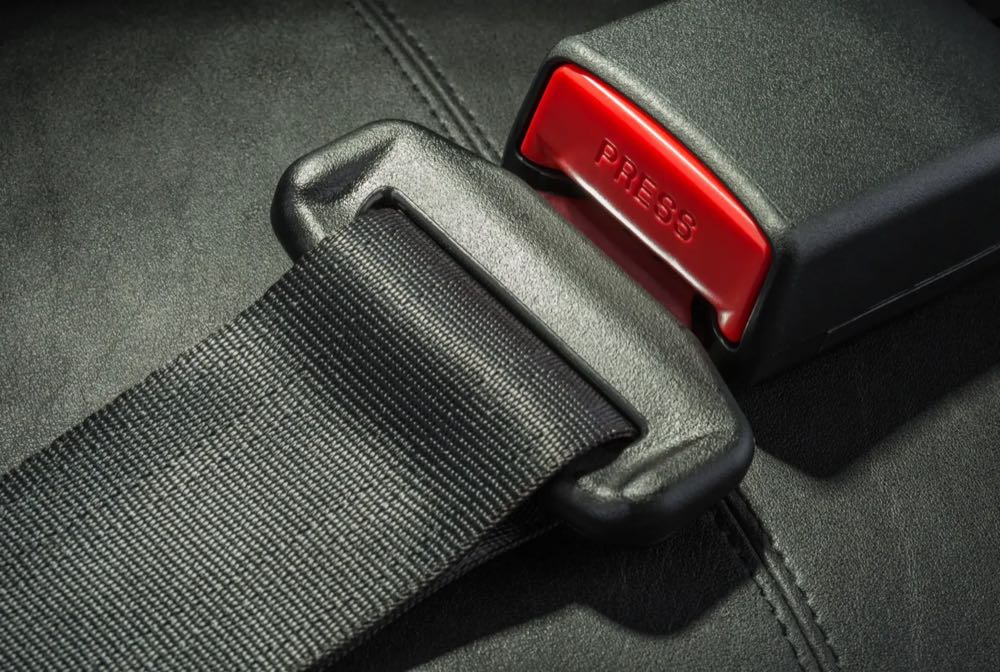 Seatbelt webbing seated in a buckle with a red release button on a dark leather seat