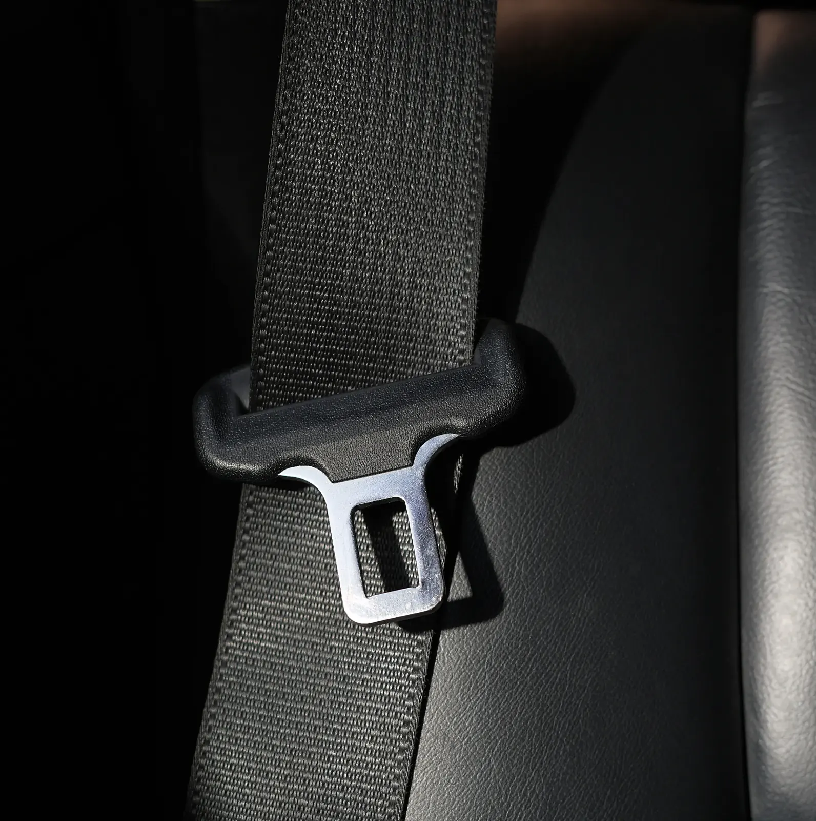 Seatbelt webbing running through an upper anchorage loop inside a dark vehicle interior