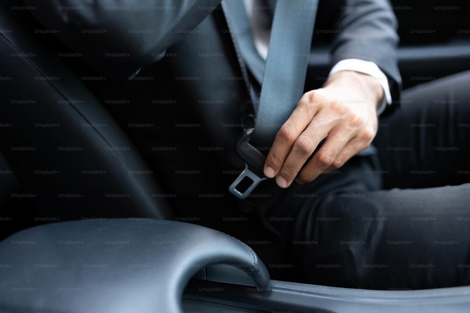 A person in a dark suit reaching for the seatbelt tongue inside a vehicle