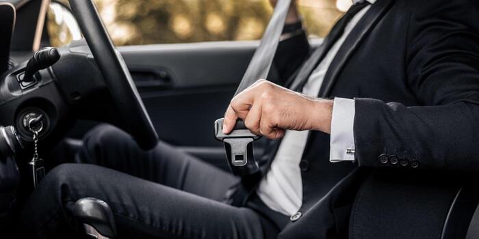 A person in business dress fastening a seatbelt in a car, seen from the side